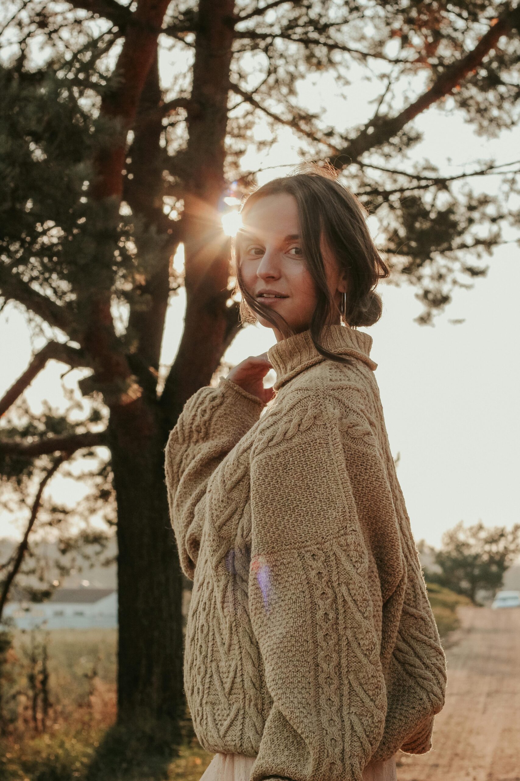 Young woman in cozy sweater standing outdoors with sun flare. Tranquil fall setting in Minsk.