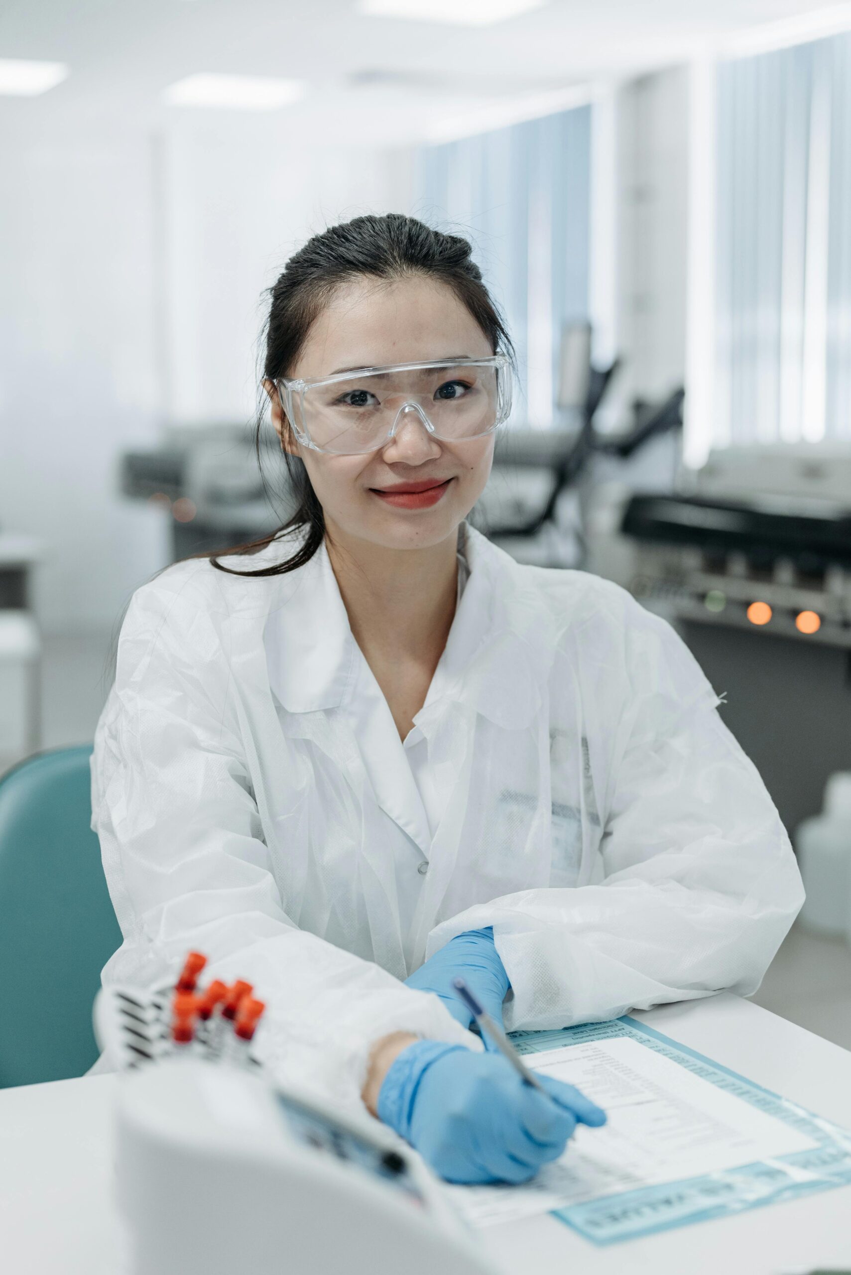 Smiling Asian female scientist with safety gear in modern laboratory environment.